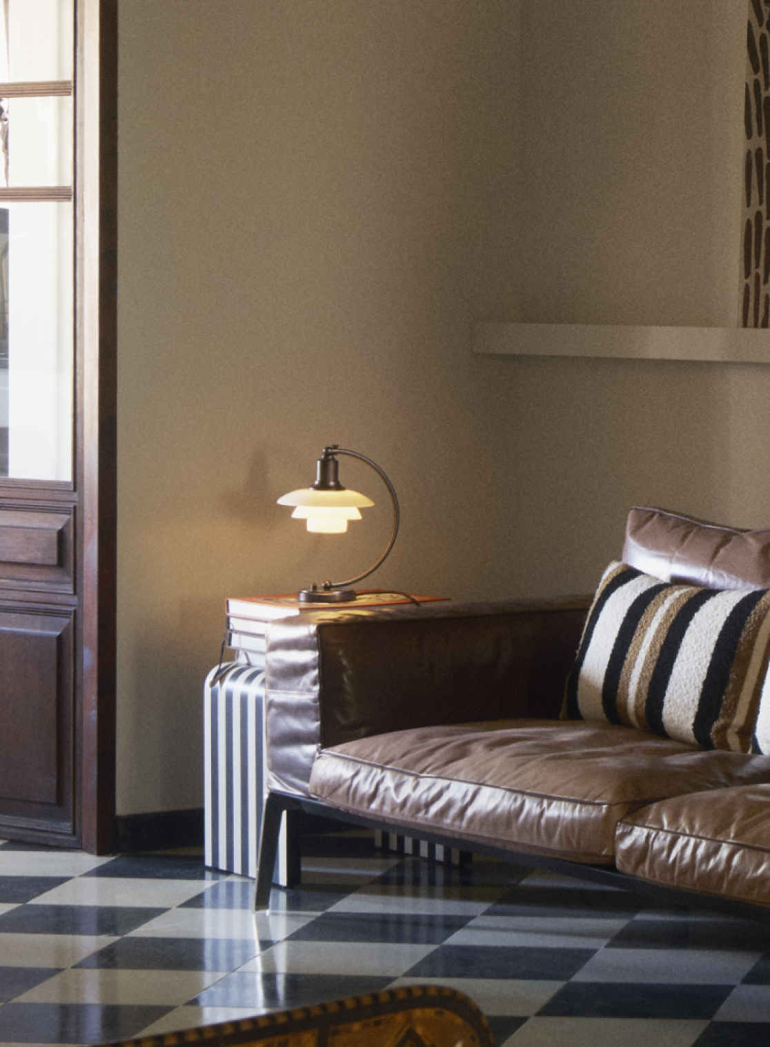 PH 2/2 Luna table lamp in aged brass next to a brown leather sofa, adding warm light, © 2025 Louis Poulsen.