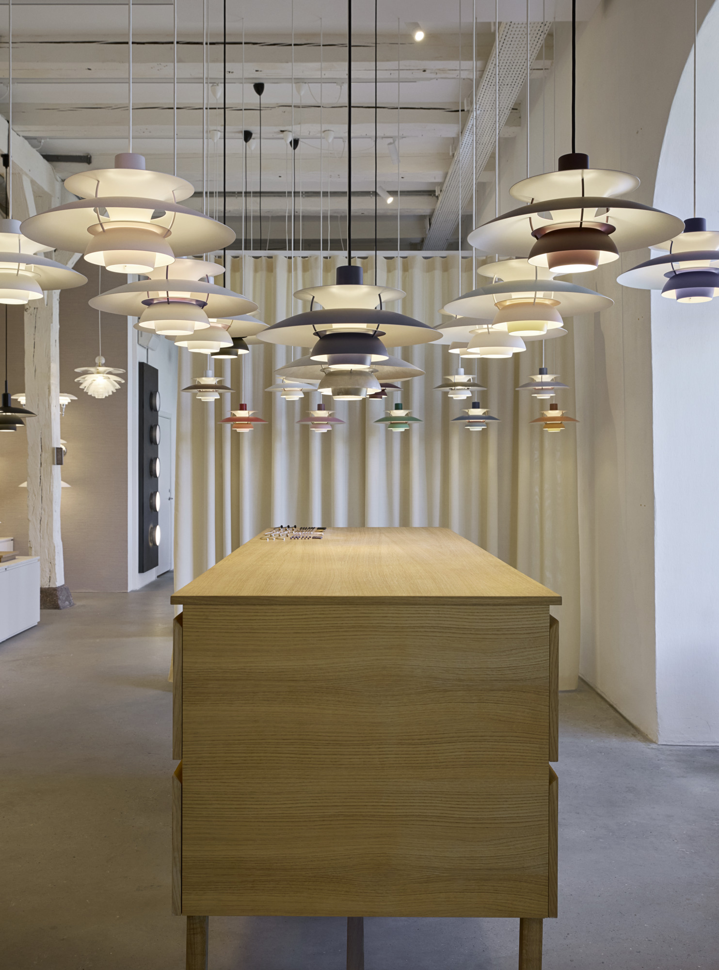 PH 5 pendant lamps in multiple colours displayed above a wooden table inside the Louis Poulsen Copenhagen showroom, © 2025 Louis Poulsen.