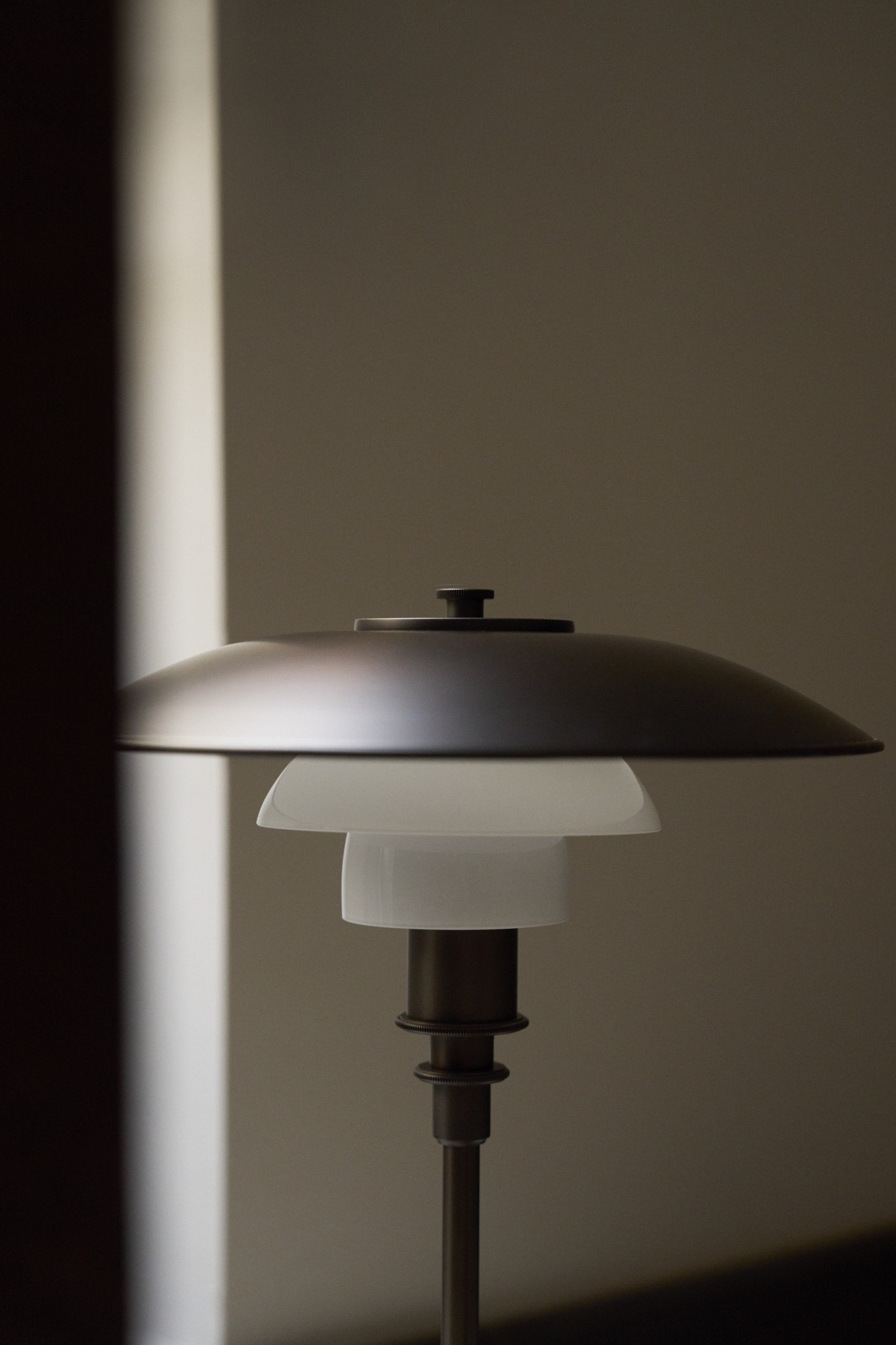 PH 3/2 Aged brass table lamp in a dimly lit room, © 2025 Louis Poulsen.