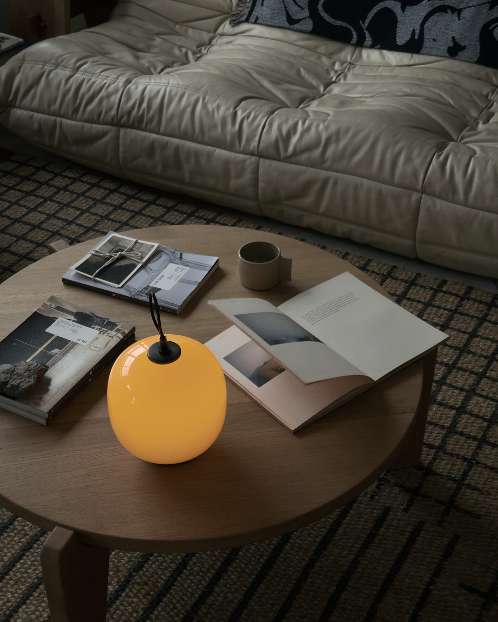 A glowing VL 45 Radiohus PortableTable Lamp on a wooden coffee table with books and a mug, © 2025 Louis Poulsen.