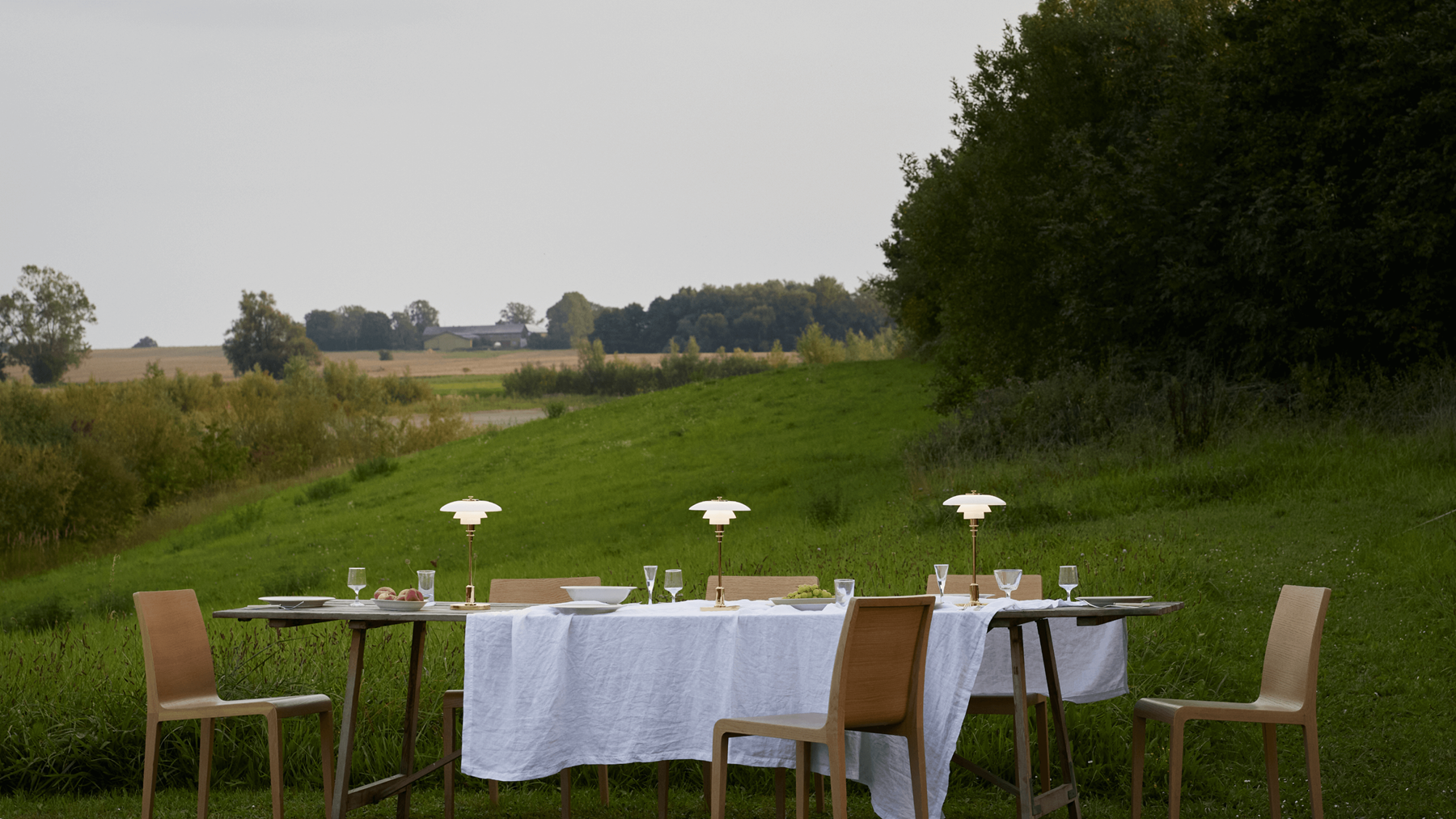 PH 2/1 Portable lamps on outdoor dining table in countryside setting, © 2025 Louis Poulsen.