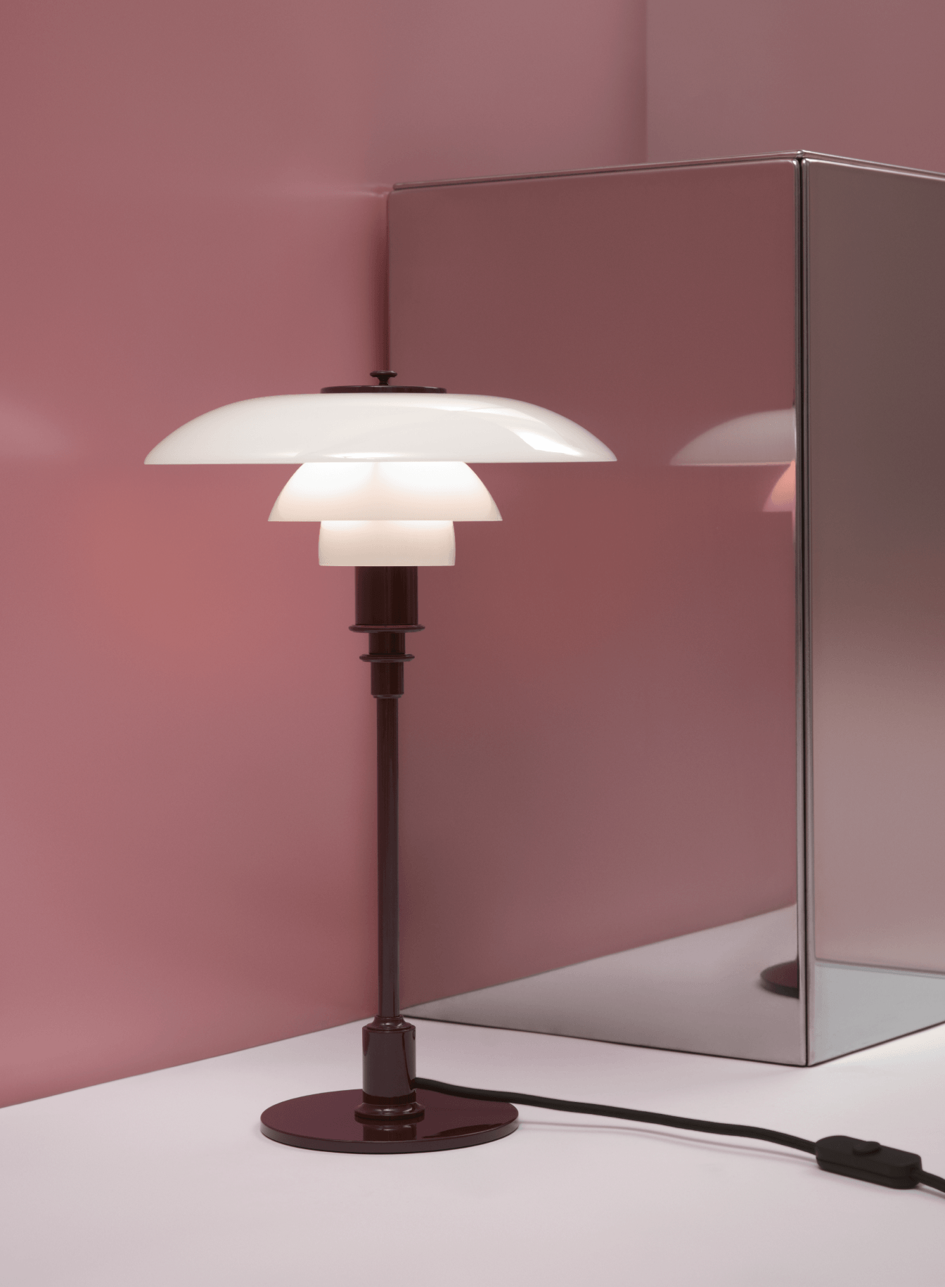 PH 3/2 Table Lamp in Glossy Burgundy with illuminated opal glass shades beside a mirrored pedestal, © 2025 Louis Poulsen.