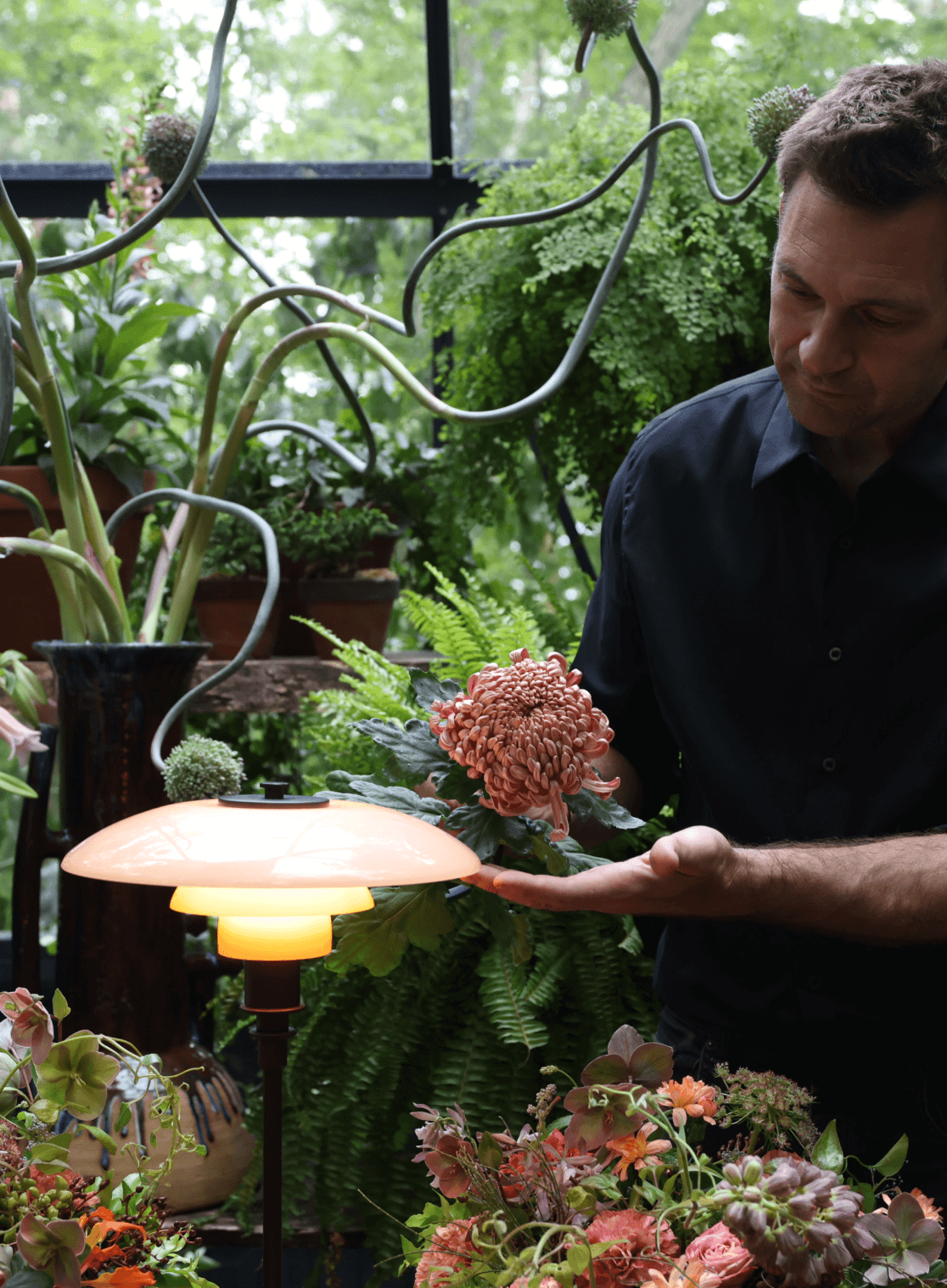 Person holding a flower near PH 3/2 table lamp in a natural setting, © 2025 Louis Poulsen.