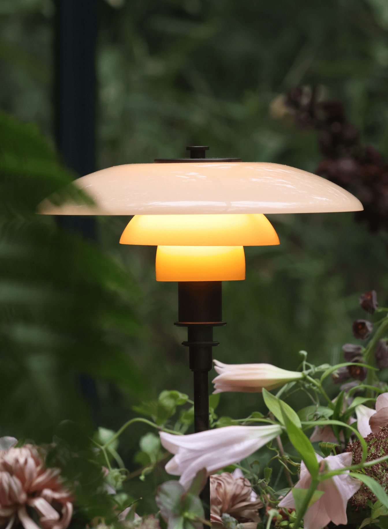 PH 3/2 table lamp casting a warm glow among plants, © 2025 Louis Poulsen.