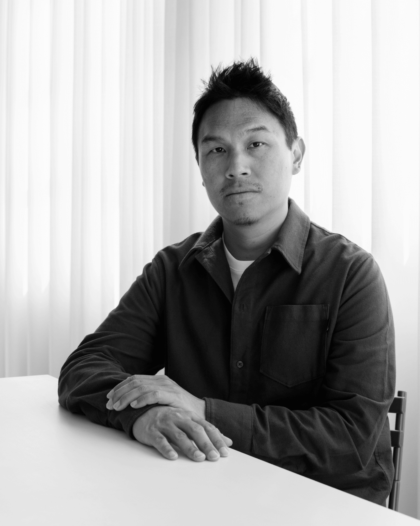 Portrait of designer Gabriel Tan seated at table with soft curtain backdrop, © 2025 Louis Poulsen.
