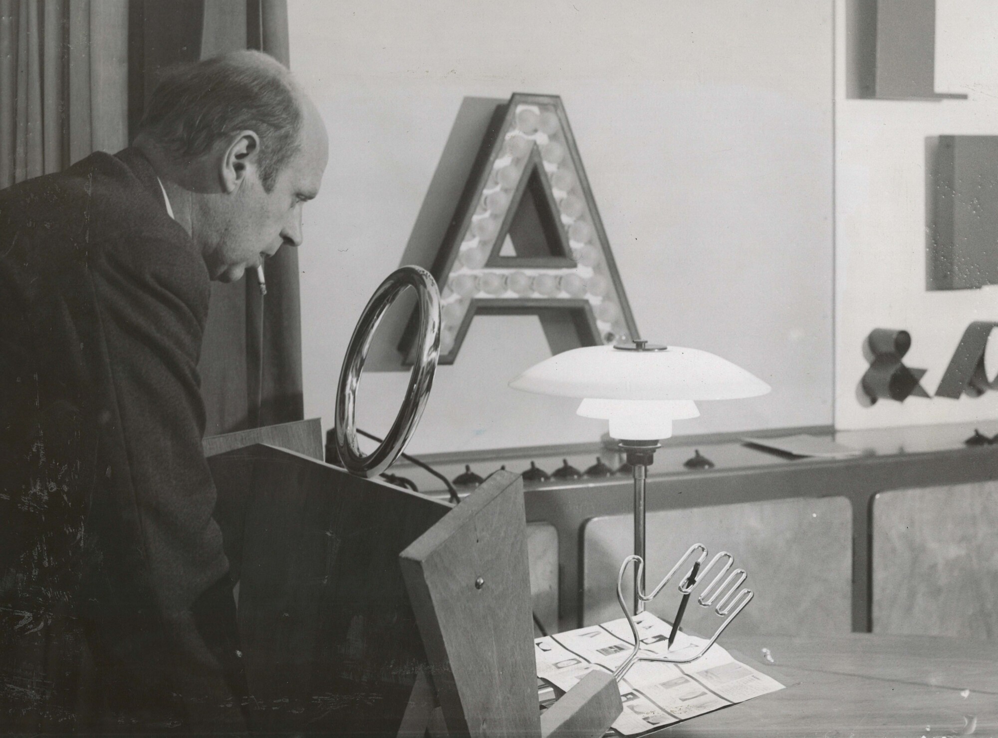Poul Henningsen examining early PH table lamp in showroom, © 2025 Louis Poulsen.
