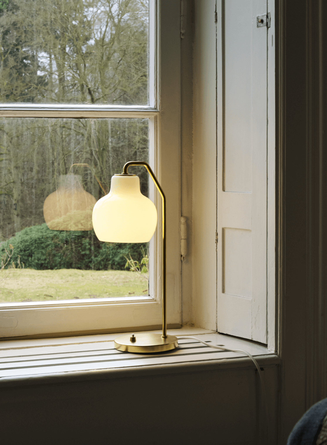VL Ring Crown table lamp in brass and opal glass on a windowsill, © 2025 Louis Poulsen.